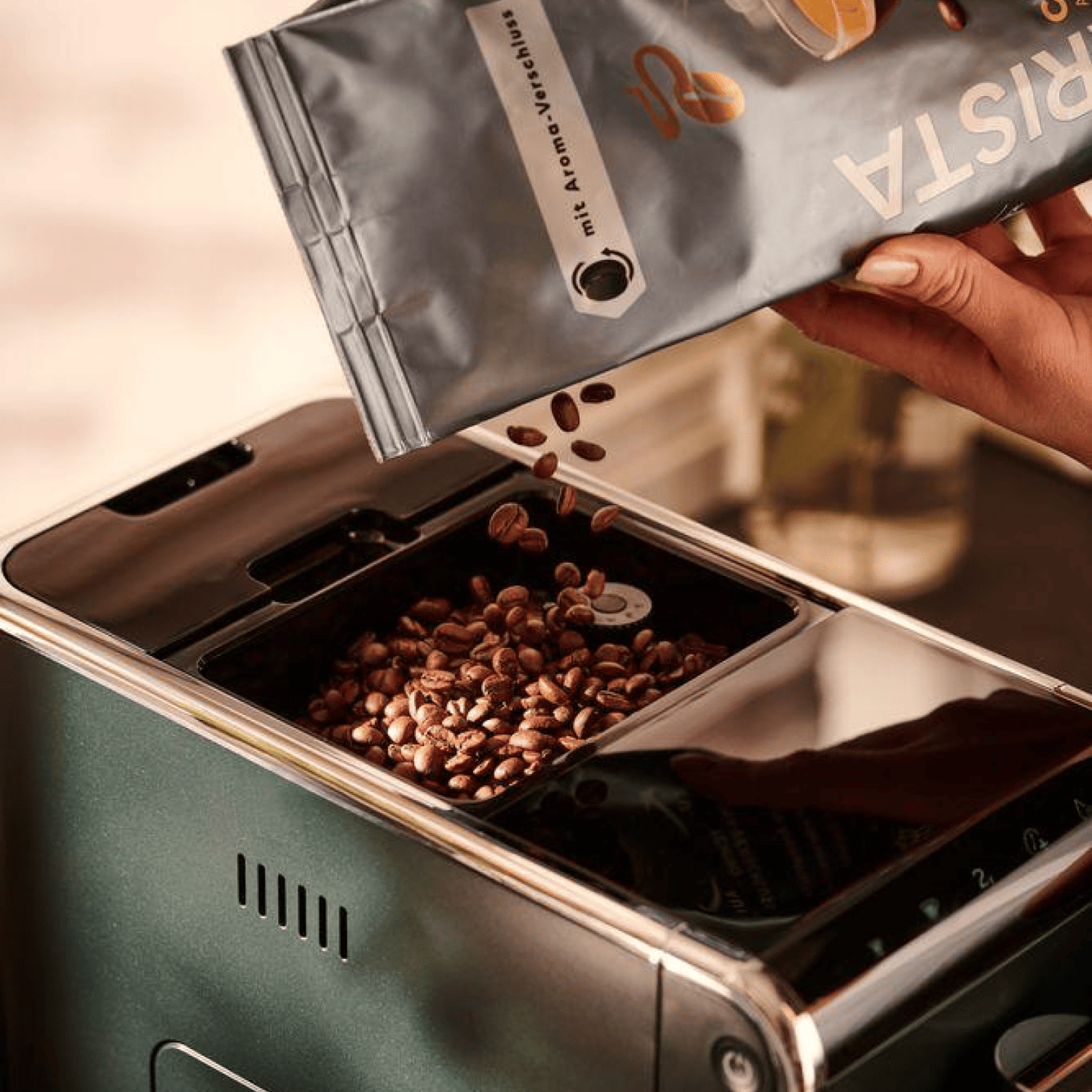 Nahaufnahme der Oberseite des Tchibo Esperto Caffè in Dark Green mit offenem Bohnenfach, während gerade neue Kaffeebohnen nachgefüllt werden.