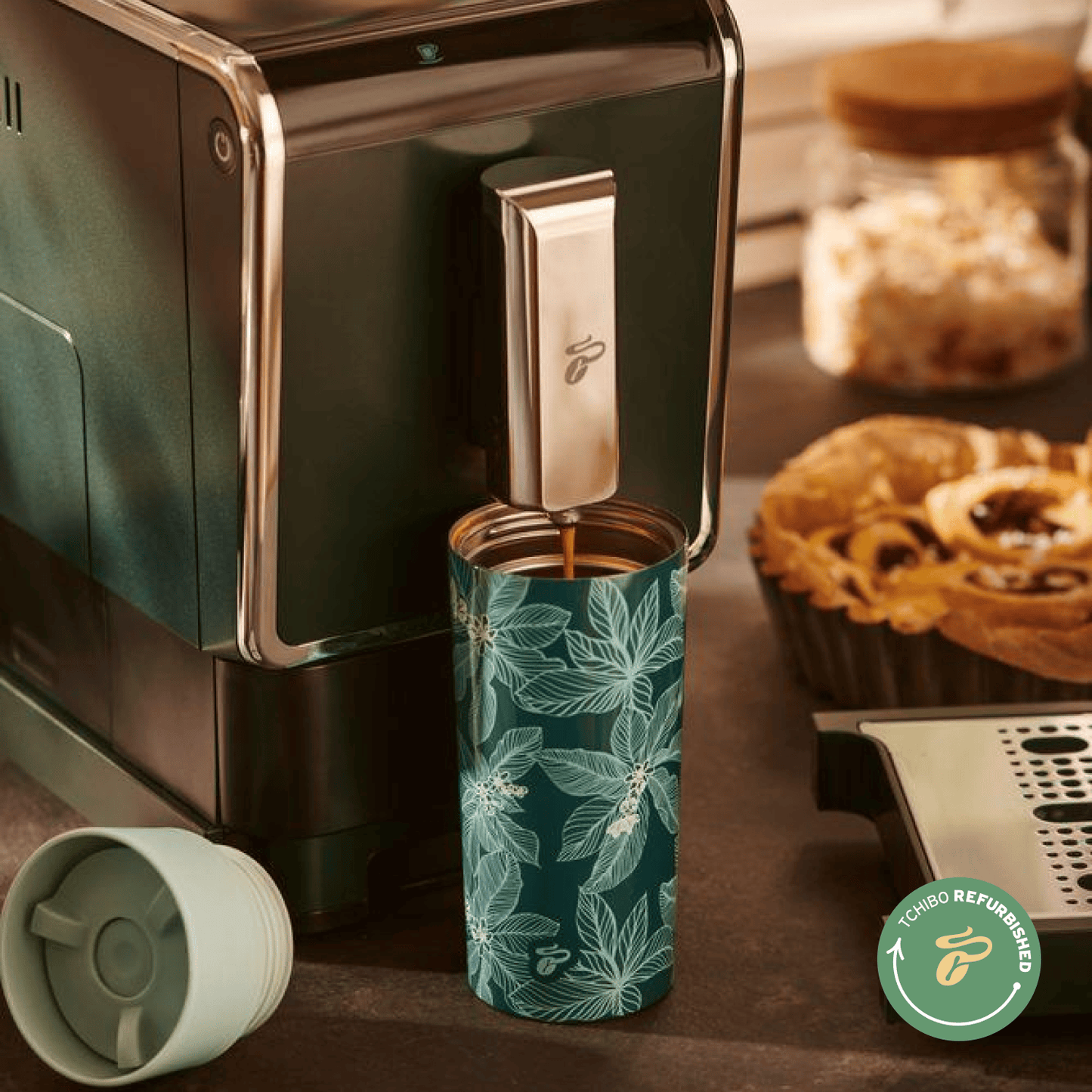 Nahaufnahme des Tchibo Esperto Caffè in Dark Green, bei dem die Abtropfschale entfernt wurde. Ein großer To-go-Becher steht unter dem Auslauf während gerade ein Kaffee gebrüht wird.