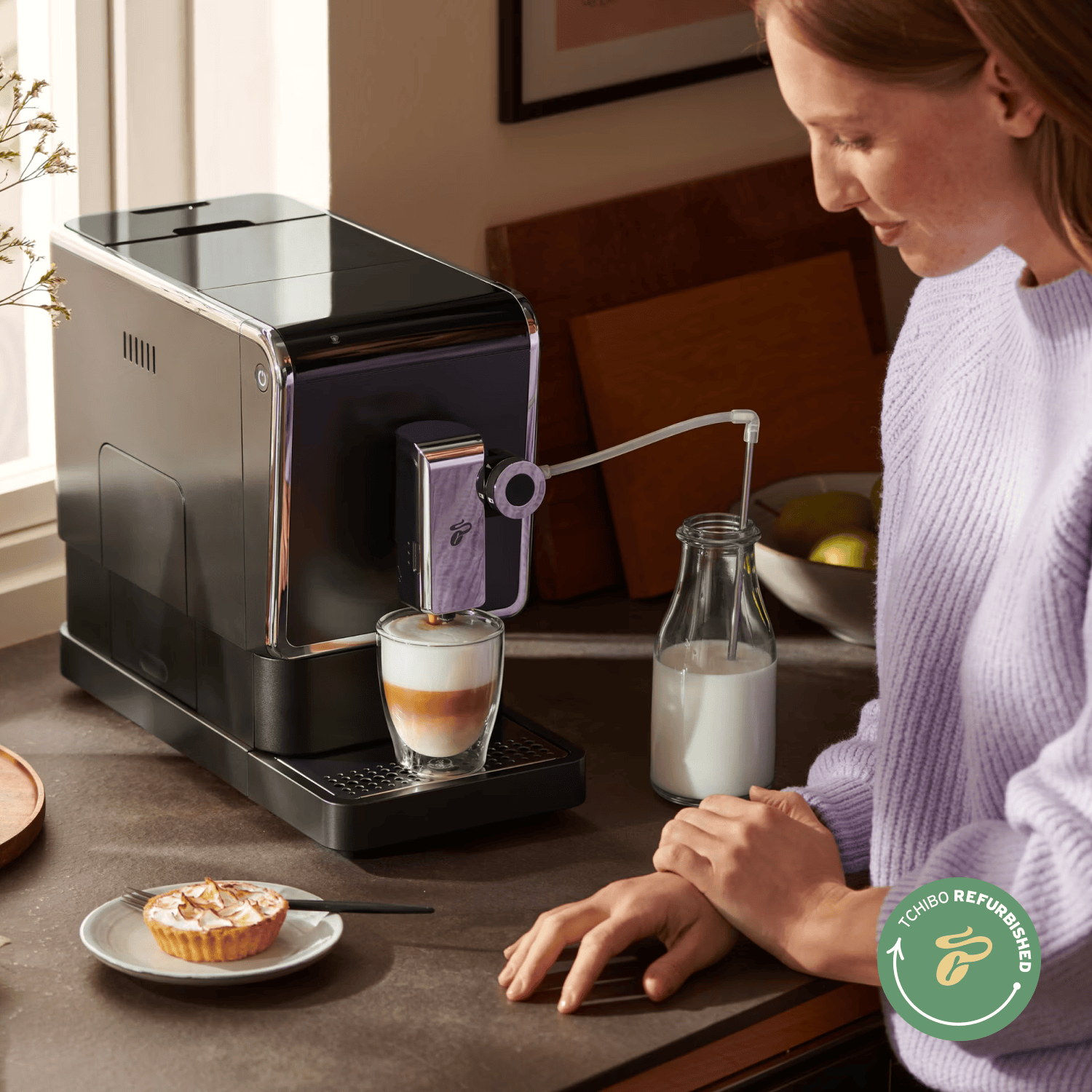 Tchibo Esperto Pro mit Milchschaum in Glas und Milchflasche, Person am Tisch mit Tarte und "Tchibo Refurbished"-Logo