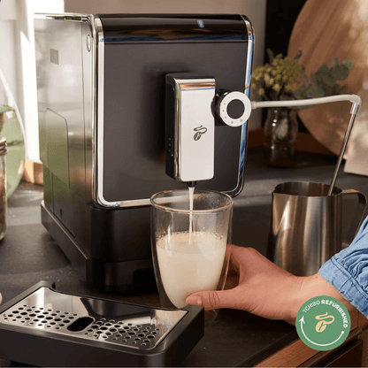 Tchibo Esperto Pro die Milchschaum im Glas zubereitet, eine Hand hält das Glas fest und man sieht das "Tchibo Refurbished"-Logo