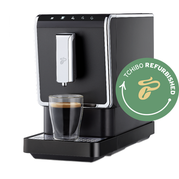 Nahaufnahme des Tchibo Esperto Caffè Vollautomaten in Anthracite, mit großem grünen Refurbished-Logo und transparentem Hintergrund. Die Aufnahme zeigt die Maschine leicht von der Seite, mit einer Kaffeetasse unter dem Auslauf.