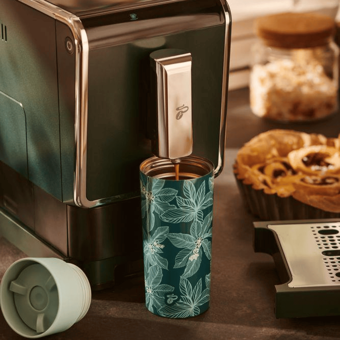 Nahaufnahme des Tchibo Esperto Caffè in Dark Green, bei dem die Abtropfschale entfernt wurde. Ein großer To-go-Becher steht unter dem Auslauf während gerade ein Kaffee gebrüht wird.