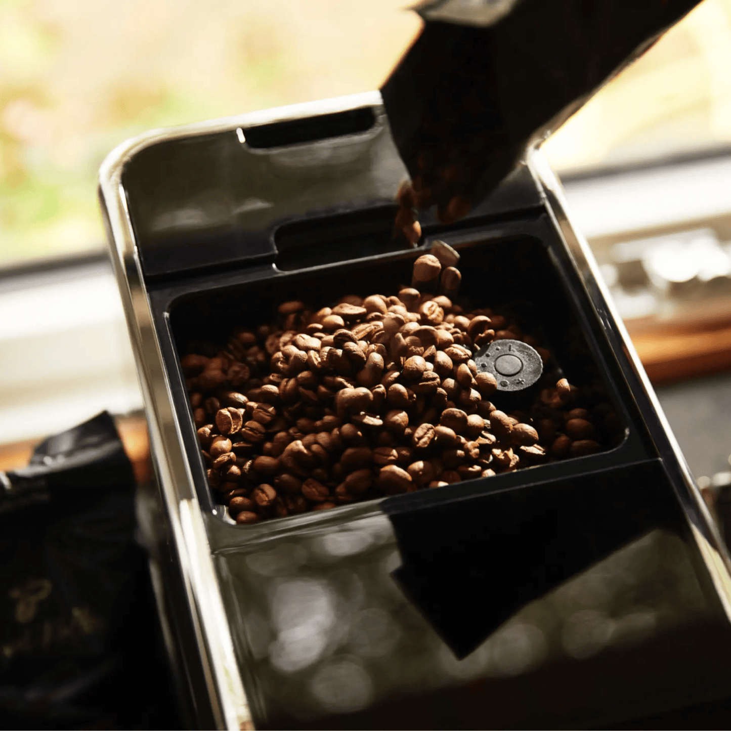 Nahaufnahme der Oberseite des Tchibo Esperto Caffè in Silver mit offenem Bohnenfach, während gerade neue Kaffeebohnen nachgefüllt werden.